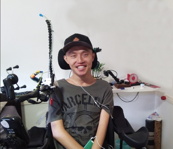 Justin Hua, sits in his chair in front of a white wall