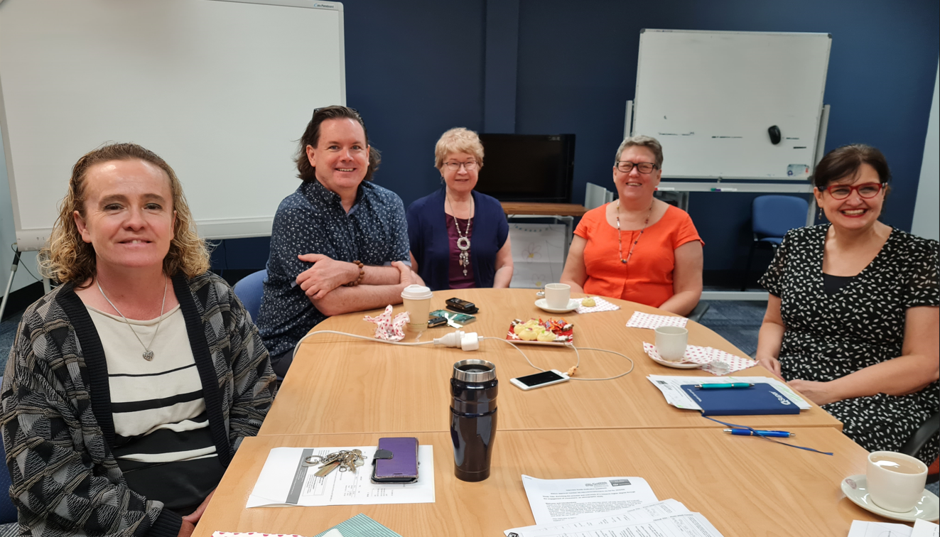 5 people sitting around a table, smiling. 