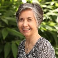 Profile image of Letitia Burridge, a woman with cropped grey hair and a patterned black and white top, in front of a green space.