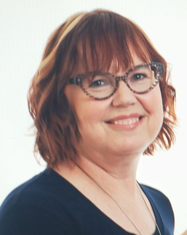 Delena Amsters, a woman with red hair with blonde streaks, wearing turtle shell style glasses and a black top.