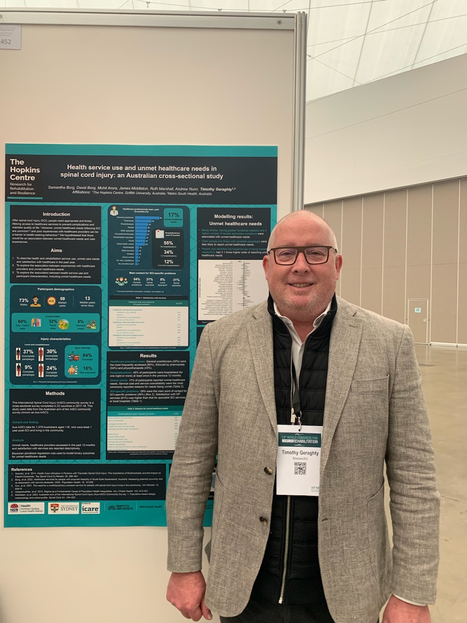 Prof Tim Geraghty, a man wearing a beige suit, standing in front of the poster he was presenting. 