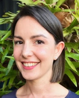 Annerley Bates, a woman with a brown bob-style haircut, wearing a blue t-shirt, in front of a vibrant green space.