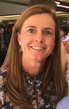 Profile photo of Louise Bassingthwaighte a woman with straight brown hair, wearing small circular earings and a floral dress.