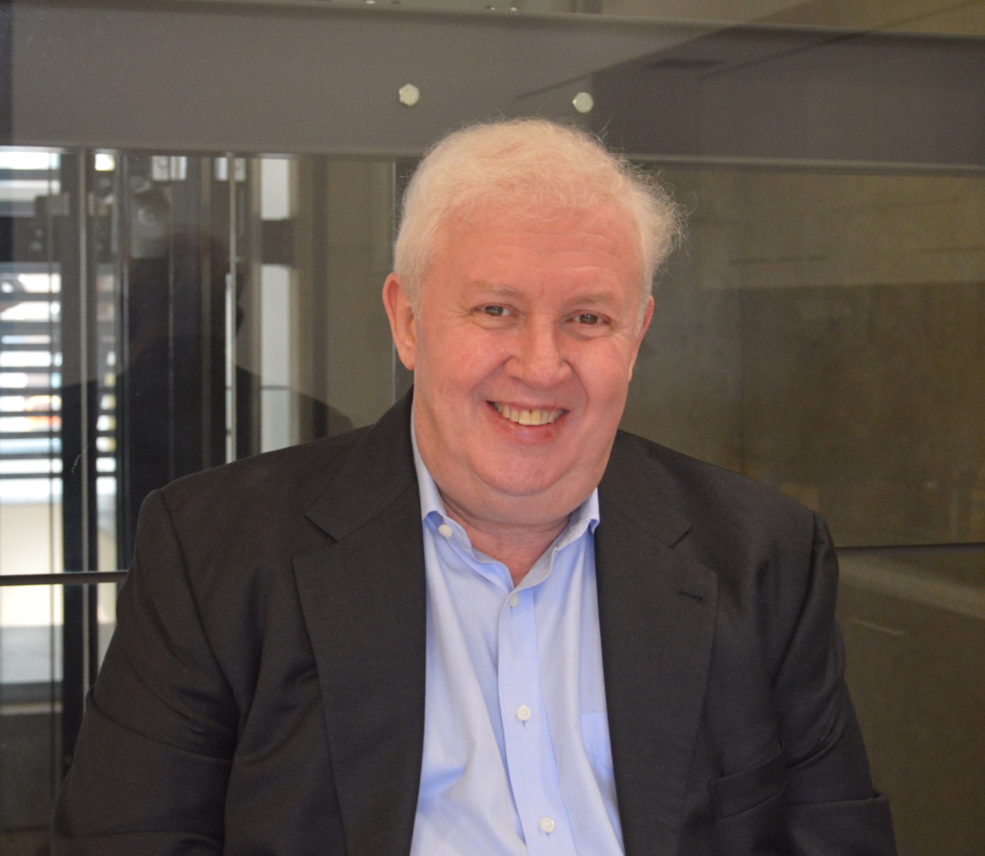 Grahame Simpson, a man with white hair, a blue collared business shirt and a grey suit jacket, smiling.